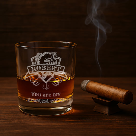 Custom rocks glass with detailed engraving of a fishing lure for fisherman gift on a bar countertop next to a cigar.